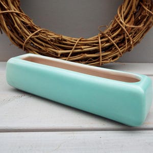 May include: A light blue ceramic planter with a rectangular shape and a white interior. The planter is ideal for displaying small plants or succulents.