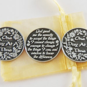 Può includere: Tre gettoni argentati con un designo floreale e le parole "One Day At A Time" su ciascuno. Il gettone centrale ha una citazione sulla serenità, l'accettazione, il coraggio e la saggezza.