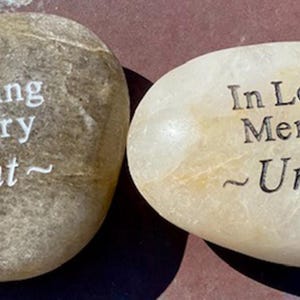 以下が含まれることがあります： 「In Loving Memory」と刻まれた、2つの滑らかで明るい色の石。1つの石には「Aunt」と刻まれ、もう1つの石には「Uncle」と刻まれています。