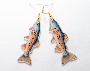 May include: A pair of fish-shaped earrings. Each earring features a colorful illustration of a fish with blue, orange, and black details. The earrings have gold-colored hooks.
