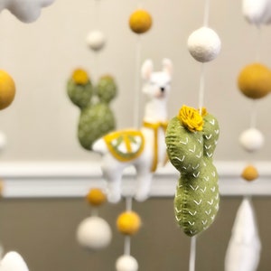 May include: A baby mobile with a llama, cacti, clouds, and felt balls in white, green, and yellow.