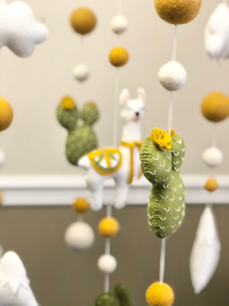 May include: A baby mobile with a llama, cacti, clouds, and felt balls in white, green, and yellow.
