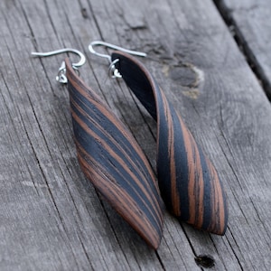 Puede incluir: Un par de pendientes largos, retorcidos, de rayas negras y marrones con ganchos plateados.