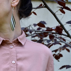 Puede incluir: Un par de pendientes largos y colgantes con un diseño a rayas en blanco, negro y verde. Los pendientes están hechos de un material ligero y tienen un estilo simple y elegante.
