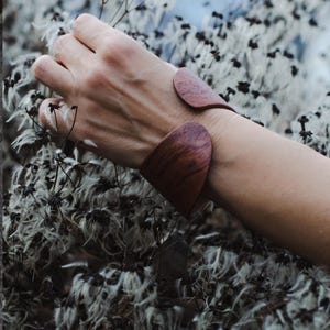 Peut inclure: Un bracelet manchette en bois de couleur brun rougeâtre. Le bracelet a un design incurvé et est porté au poignet. Le fond présente des fleurs blanches et noires.