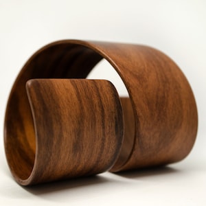 Puede incluir: Una escultura de madera hecha de dos piezas de madera curvas. La madera tiene un rico color marrón y un patrón de veta de madera natural.