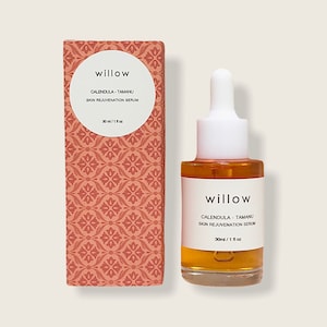 May include: A 30 ml bottle of willow calendula-tamanu skin rejuvenation serum. The bottle is clear glass with a white dropper and a white label with the product name and ingredients. The bottle is sitting on a light brown surface.