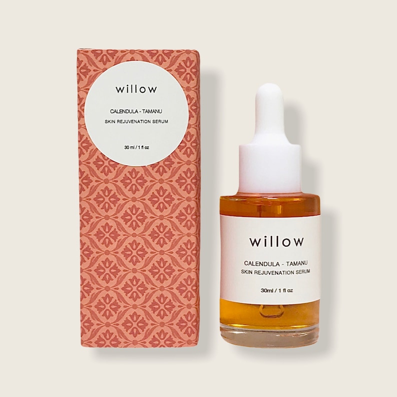 May include: A 30 ml bottle of willow calendula-tamanu skin rejuvenation serum. The bottle is clear glass with a white dropper and a white label with the product name and ingredients. The bottle is sitting on a light brown surface.