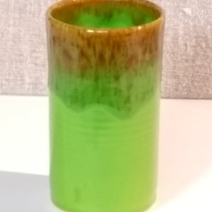 May include: A green ceramic mug with a brown glaze on the top rim. The mug is cylindrical in shape and has a smooth, glossy finish.