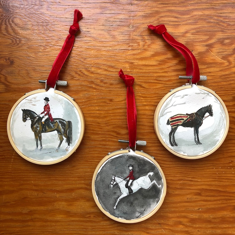 K&ouml;nnte beinhalten: Drei runde Ornamente mit aquarellierten Gem&auml;lden zum Thema Reiten. Jedes Ornament zeigt ein Pferd und einen Reiter oder ein Pferd mit einer Decke. Die Ornamente sind in Holzreifen gefasst und haben rote Samtbandschlaufen.
