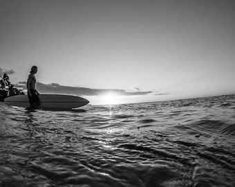 Black and White vintage style photo of a surfer entering the water to go surfing in Hawaii during sunset.