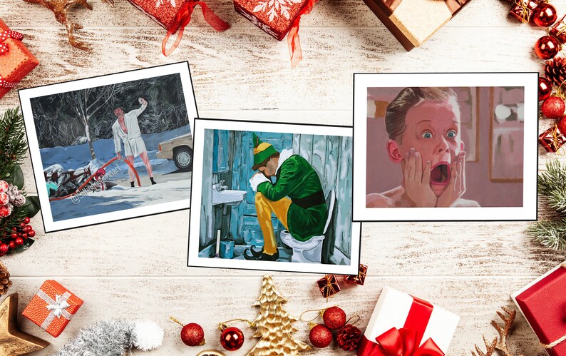 May include: Three rectangular art prints featuring movie scenes. The left print shows a person in a white robe outdoors in snow. The center print depicts a person in a green and yellow elf costume sitting on a toilet. The right print shows a close-up of a person with hands on their face in a shocked expression.