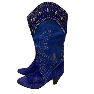 May include: Blue suede cowboy boots with silver studs and a lace pattern. The boots have a pointed toe and a low heel.