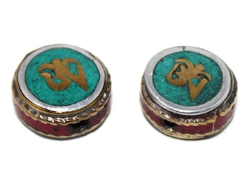 May include: Two round, decorative beads with a gold Om symbol on a turquoise background. The beads are surrounded by a silver band and a red border.