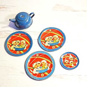 May include: A vintage blue metal teapot and four matching tin plates. The plates have a red background with a cartoon illustration of three figures in a boat. The plates have a blue rim.