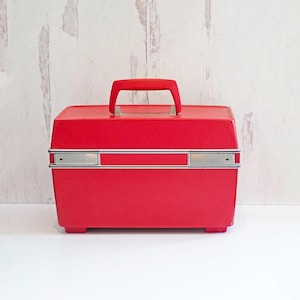 May include: A bright red vintage travel case with a silver handle and trim. The case has a rectangular shape and a smooth, glossy finish.