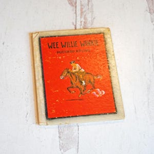 May include: A vintage children's book titled "Wee Willie Winkie" by Rudyard Kipling. The cover is a vibrant red with an illustration of a person riding a brown horse. The book has a worn, aged appearance.