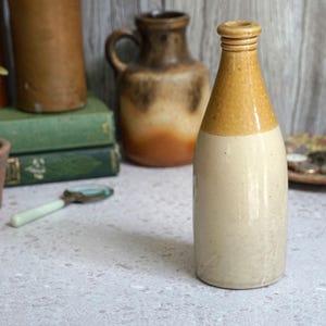 May include: A vintage stoneware bottle with a brown and white glaze. The bottle has a rounded body and a narrow neck.