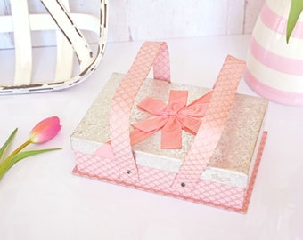 May include: A pink and silver gift box with a bow and handles. The box is decorated with a pattern of small circles.
