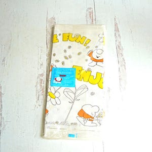 May include: A vintage white tablecloth with a cartoon design featuring the words "ENJOY" and "FUN!" in yellow. The design includes cartoon characters, daisies, and other floral elements. The tablecloth measures 54 x 54 inches.
