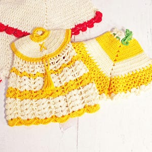 May include: Two crocheted garments, one white with red trim and one yellow and white with a tassel.