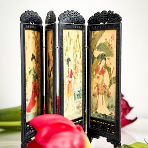 Peut inclure: Un petit paravent noir à quatre panneaux. Chaque panneau présente une peinture d'une femme en tenue asiatique traditionnelle. Une tulipe rouge est au premier plan.