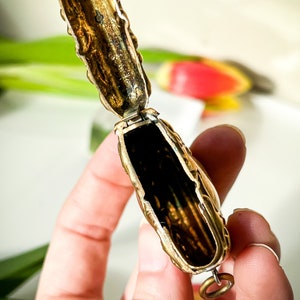 K&ouml;nnte beinhalten: Ein verziertes, goldfarbenes, Scharnier-Medaillon mit einem detaillierten Blumendesign. Das Medaillon ist ge&ouml;ffnet und zeigt ein leeres Inneres. Es hat einen kleinen Ring, der an der Unterseite befestigt ist.