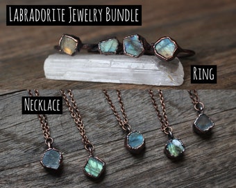 May include: Labradorite jewelry bundle featuring rings and necklaces. The rings have a copper-colored band with a raw, multi-colored stone. The necklaces have a copper chain with a similar stone pendant. The text "Labradorite Jewelry Bundle", "Ring", and "Necklace" are visible.