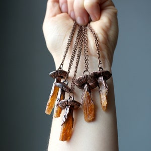 May include: A set of five copper necklaces with orange crystal pendants. Each pendant is shaped like a mushroom with a copper cap and a long, thin crystal stem.