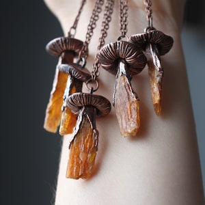May include: A set of five copper mushroom necklaces with amber crystal pendants. Each necklace features a detailed copper mushroom cap and a long, slender amber crystal pendant.