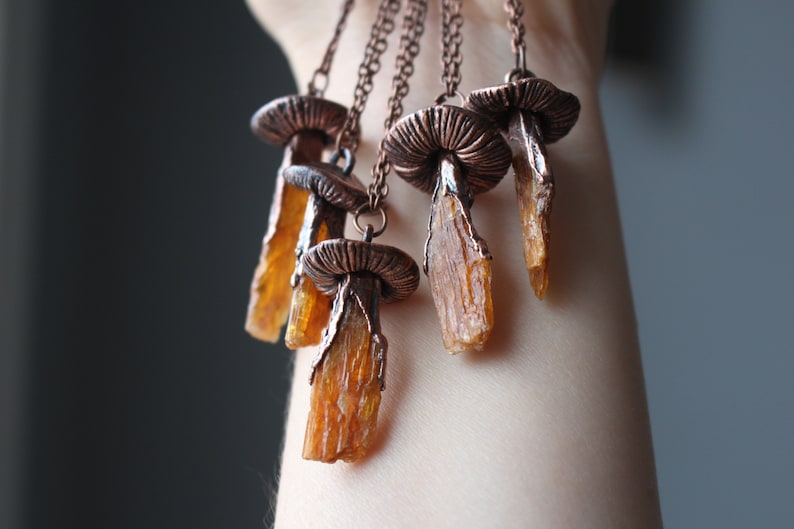 May include: A set of five copper mushroom necklaces with amber crystal pendants. Each necklace features a detailed copper mushroom cap and a long, slender amber crystal pendant.