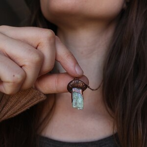 May include: A copper pendant necklace with a light green crystal. The crystal is a rectangular shape and is set in a copper frame. The necklace is on a chain.