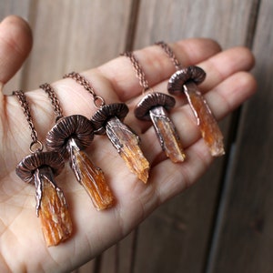 May include: Five copper mushroom necklaces with orange crystal pendants. Each necklace features a detailed copper mushroom cap and a long, slender orange crystal pendant.