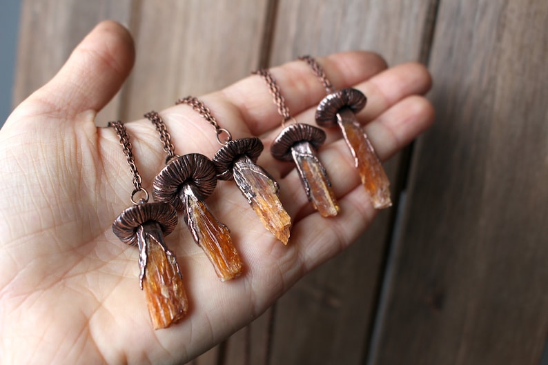 May include: Five copper mushroom necklaces with orange crystal pendants. Each necklace features a detailed copper mushroom cap and a long, slender orange crystal pendant.