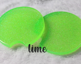 May include: Two round green glitter coasters with a cut-out for a cup. The coasters are labeled "lime".