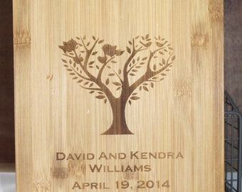 May include: A light brown bamboo cutting board with a laser engraved design of a tree with birds and the text "David and Kendra Williams April 19, 2014".