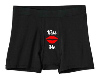 May include: Black boxer shorts with a red lip print and the text "Kiss Me" in white.