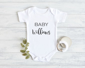 May include: White baby onesie with black text that reads "BABY Williams".