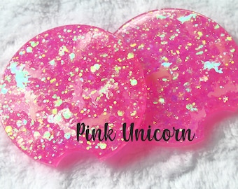 May include: Two pink round coasters with iridescent glitter and white unicorn silhouettes. The coasters have the text "Pink Unicorn" printed on them.