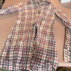 Op de afbeelding: Een geruit shirt met lange mouwen in een klassiek patroon van rood, wit en bruin. Het shirt heeft een knoopsluiting, kraag en manchetten. De stof lijkt een lichtgewicht katoen of mix te zijn, geschikt voor vrijetijdskleding. Ongeveer 80 cm lang.