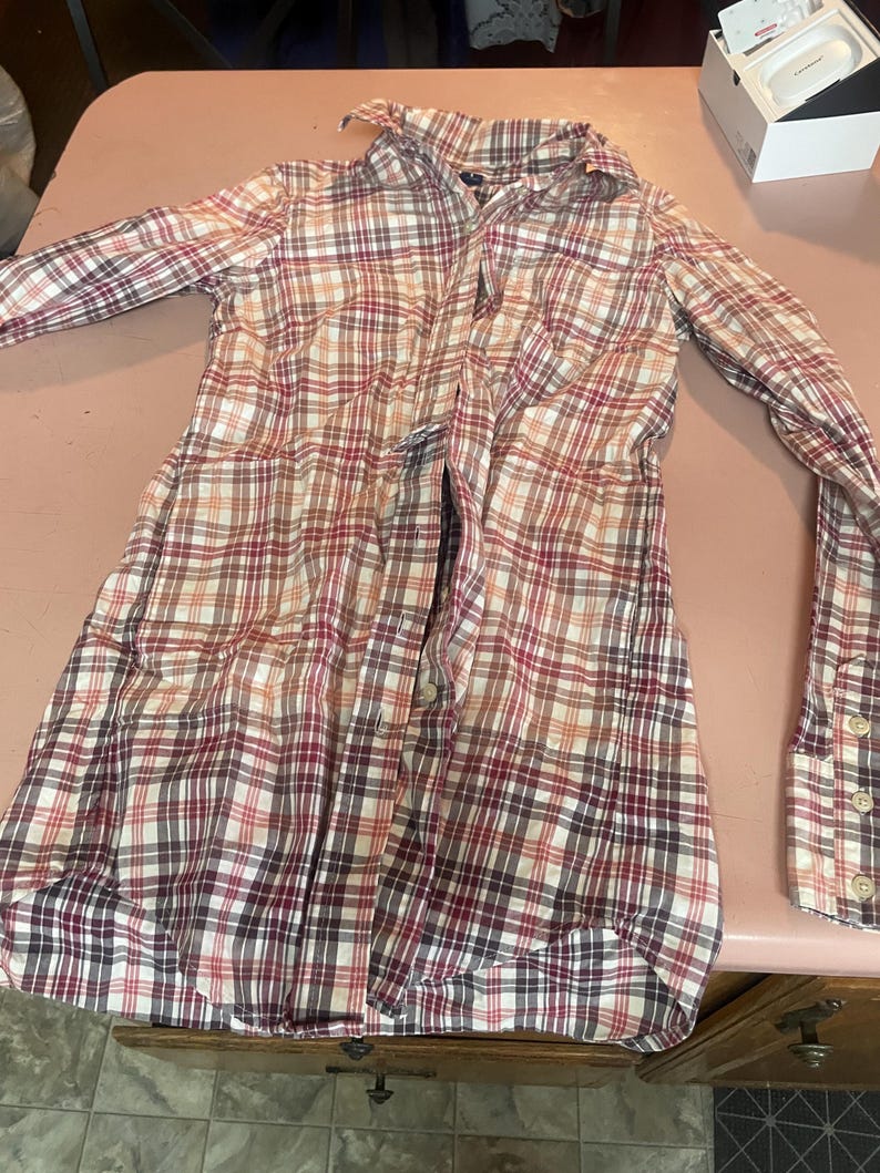 Op de afbeelding: Een geruit shirt met lange mouwen in een klassiek patroon van rood, wit en bruin. Het shirt heeft een knoopsluiting, kraag en manchetten. De stof lijkt een lichtgewicht katoen of mix te zijn, geschikt voor vrijetijdskleding. Ongeveer 80 cm lang.