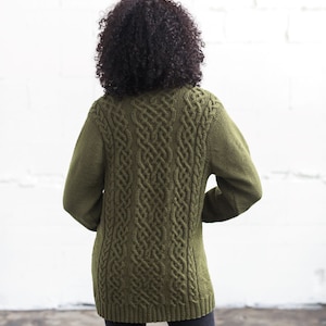May include: A green cable knit sweater with a long, loose fit. The sweater features a traditional cable knit pattern.