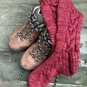 May include: A pair of brown leather hiking boots with yellow and black laces, next to a pair of red knitted socks.