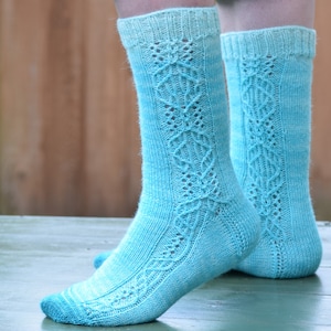 Könnte beinhalten: Ein Paar hellblaue Stricksocken mit einem Spitzenmuster. Die Socken sind aus einem Farbverlaufsgarn gefertigt, das von einem dunkleren Blau zu einem helleren Blau übergeht.
