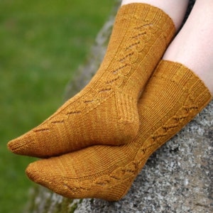 Pode incluir: Um par de meias de tricô amarelo mostarda com um delicado padrão de cabo. As meias são feitas com um fio macio e têm um ajuste confortável.
