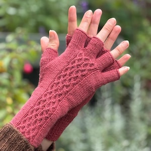 May include: Dusty rose-coloured knitted fingerless gloves. The gloves have a diamond pattern on the back and are made from a soft, textured yarn. Designed to keep hands warm while leaving fingers free, they are ideal for cooler weather.