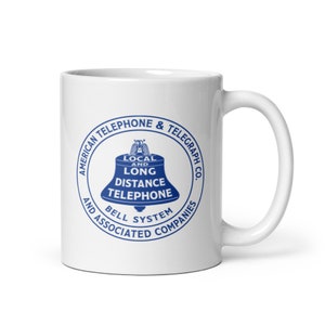 May include: White ceramic mug with a blue logo that reads "American Telephone & Telegraph Co. Local and Long Distance Telephone Bell System and Associated Companies".