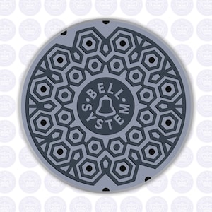 May include: A gray metal manhole cover with a black geometric pattern and the text "BELL. SYSTEM." in the center. The cover has a raised bell symbol.