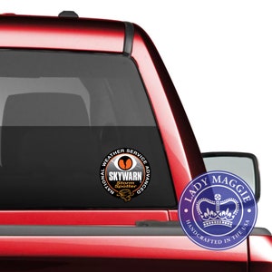 May include: A red pickup truck with a black window sticker that says "National Weather Service Advanced SKYWARN Storm Spotter". The sticker has a black and orange design with a stylized eye and lightning bolt. A blue and white sticker with a crown and the text "Lady Maggie Handcrafted in the USA" is on the truck's rear passenger side window.