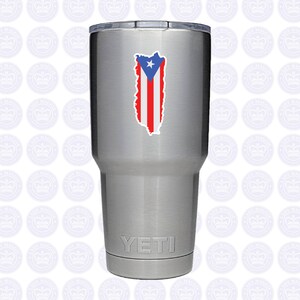May include: A silver Yeti tumbler with a sticker of the Puerto Rican flag on the front. The flag is red, white, and blue with a star in the upper left corner.
